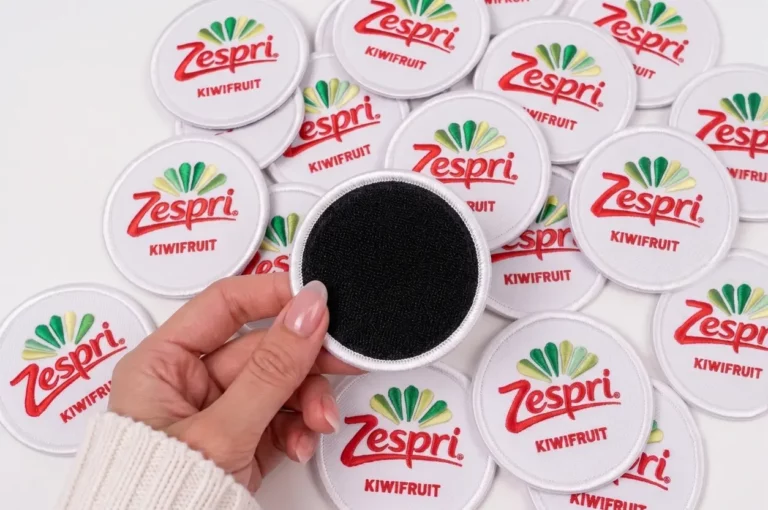 Primer plano táctico y detallado de la aplicación de un parche bordado personalizado de Bordado Point con fijación de velcro macho sobre una chaqueta de uniforme, mostrando el reverso de los ganchos y el logo.
